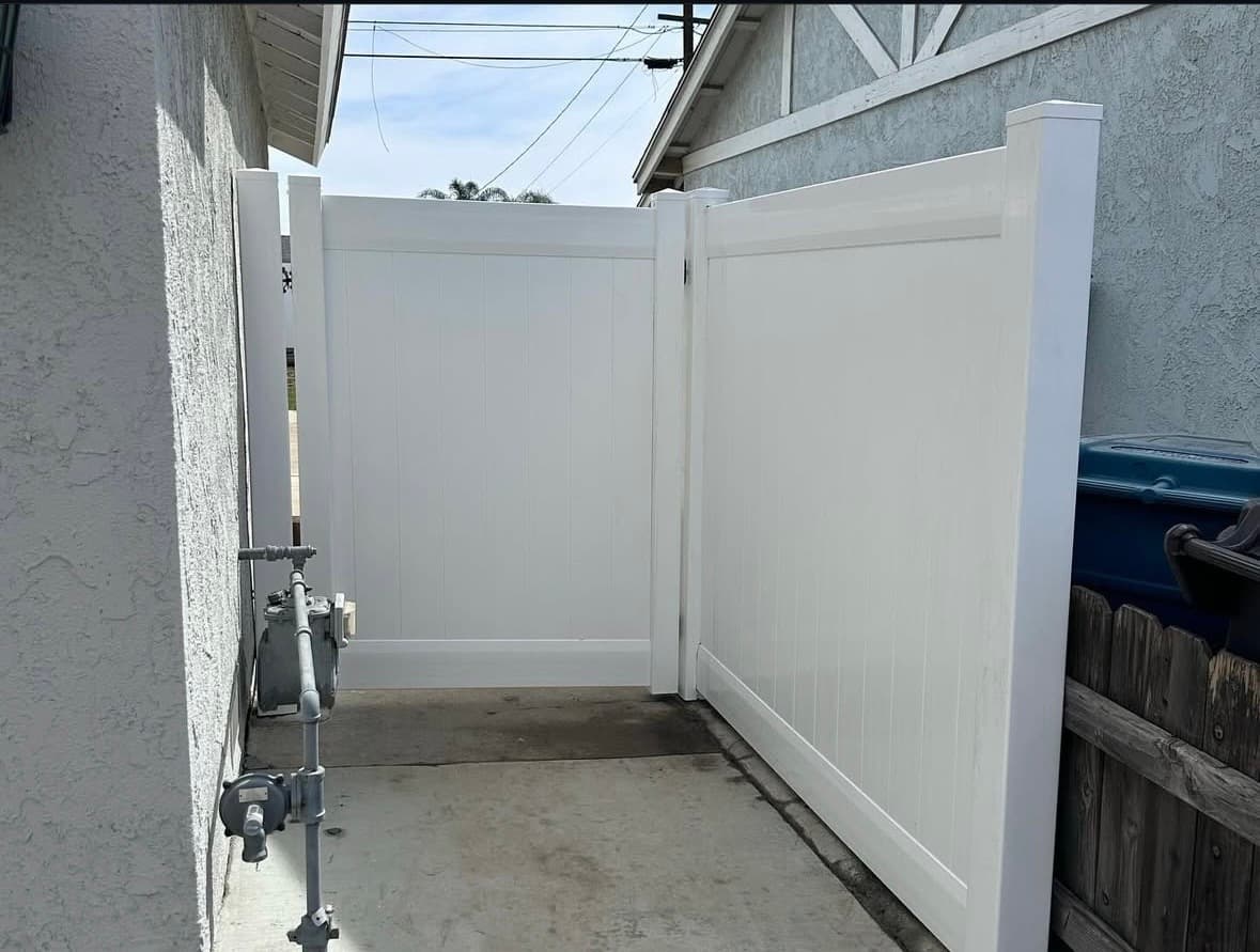 Tall white vinyl privacy gate and fence section installed between two stucco houses on concrete.