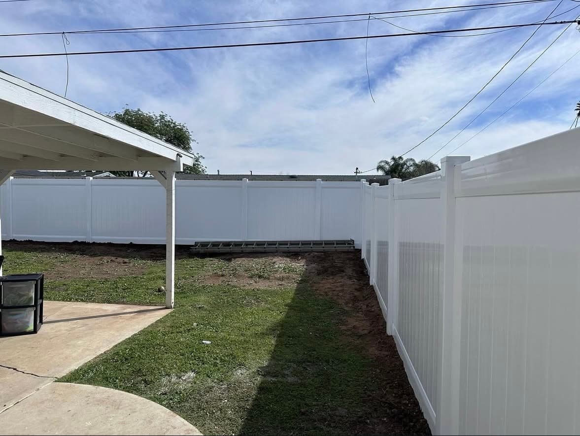 Tall white vinyl fence bordering a grassy backyard with a ladder and patio overhang.